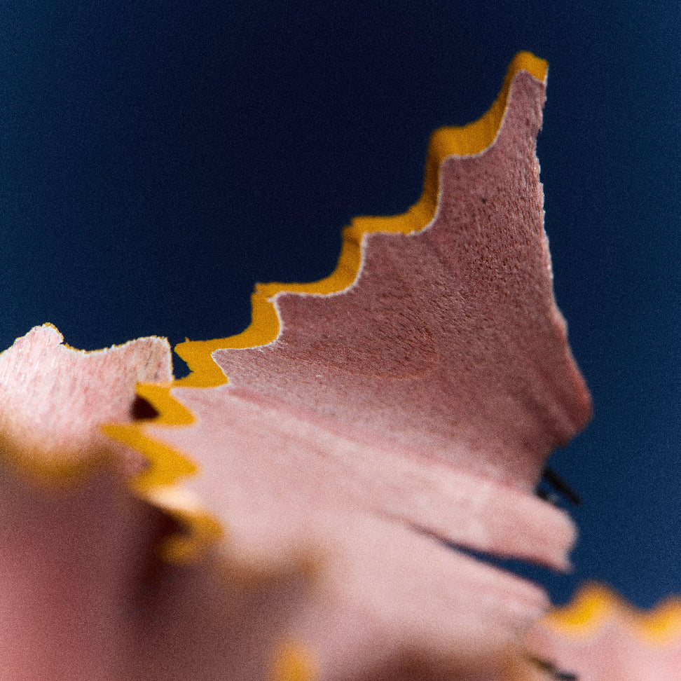 Close-up macro shot of pink pencil shavings with a bright yellow core edge against a dark blue background.